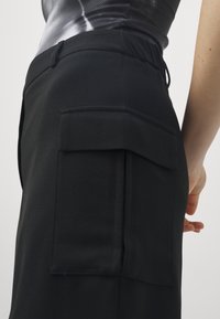 Pantalon de sport noir avec une poche cargo sur le côté, une taille élastique et une texture de tissu lisse. Coupe ajustée avec des détails de conception fonctionnels.