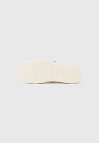 Semelle de chaussure en caoutchouc blanc avec des rainures texturées, dotée d'un logo en relief et d'un motif circulaire. Fini lisse, conçu pour l'adhérence et la traction.
