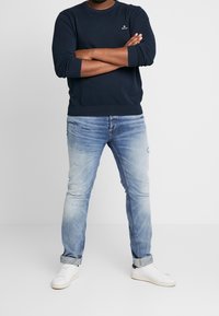 Marineblauwe sweatshirt, ontspannen pasvorm, met geribbelde manchetten. Lichtblauwe distressed jeans met opgerolde manchetten, gecombineerd met witte sneakers.