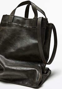 Svart läder tote-väska med två robusta handtag, ett långt justerbart rem och en mjuk, texturerad yta. Minimalistisk design, rymligt inre.