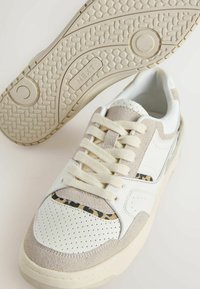 Valged ja heleda beeziga seemis- ja nahkjalatsid, millel on perforatsioonid, siledad paelad ja tekstureeritud kummitald. Lehviku mustriga aktsent.