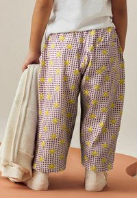 Lila Karo-Hosen mit einem gelben Smiley-Blumenmuster, im lässigen Schnitt und mit Seitentaschen, kombiniert mit einem hellen off-white Sweatshirt.
