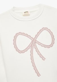 Hvid sweatshirt med et stort, pink bue-design med bølgede kanter. Stoffet ser blødt ud med en rund halsudskæring og ribbede manchetter.