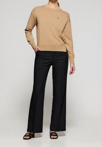 Pull en laine beige à col rond, associé à un pantalon large noir et des sandales noires ornées d'une boucle logo dorée.