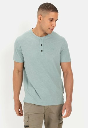 Lyseblå kortærmet Henley-skjorte med rund halsudskæring, tre-knap placket og subtil tekstur. Bæres med khaki cargo-shorts.
