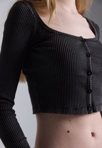Black, ribbed long-sleeve crop top featuring a wide neckline and front button closure. Material appears soft with a slight sheen.