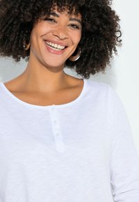 Chemise blanche à manches longues en tissu doux, avec un col rond et une patte de boutonnage à trois boutons à l'avant. Design texturé et léger.