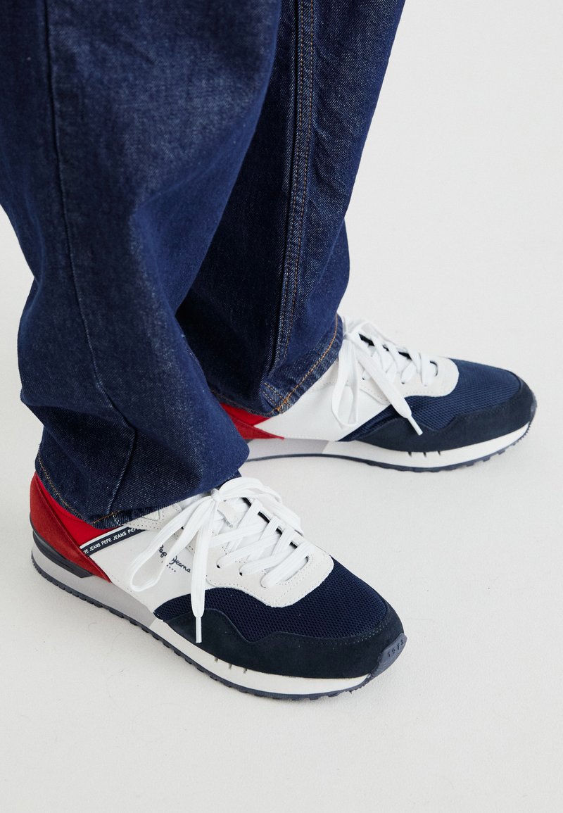 Sportliche Sneakers in Marineblau und Weiß mit roten Akzenten, aus Mesh und Wildleder, ausgestattet mit weißen Schnürsenkeln und einer strukturierten Gummisohle.