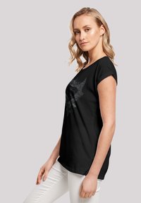 Black t-shirt with a round neckline and rolled short sleeves, featuring a graphic design in gray, worn with white pants.