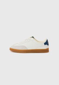 White sneakers with a smooth leather upper, tan gum rubber sole, subtle grey accents, and green and blue detailing on the heel.