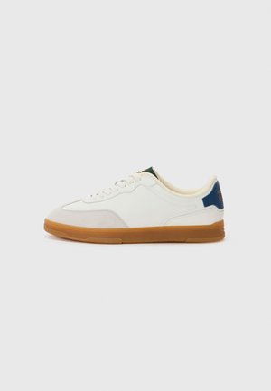 White sneakers with a smooth leather upper, tan gum rubber sole, subtle grey accents, and green and blue detailing on the heel.