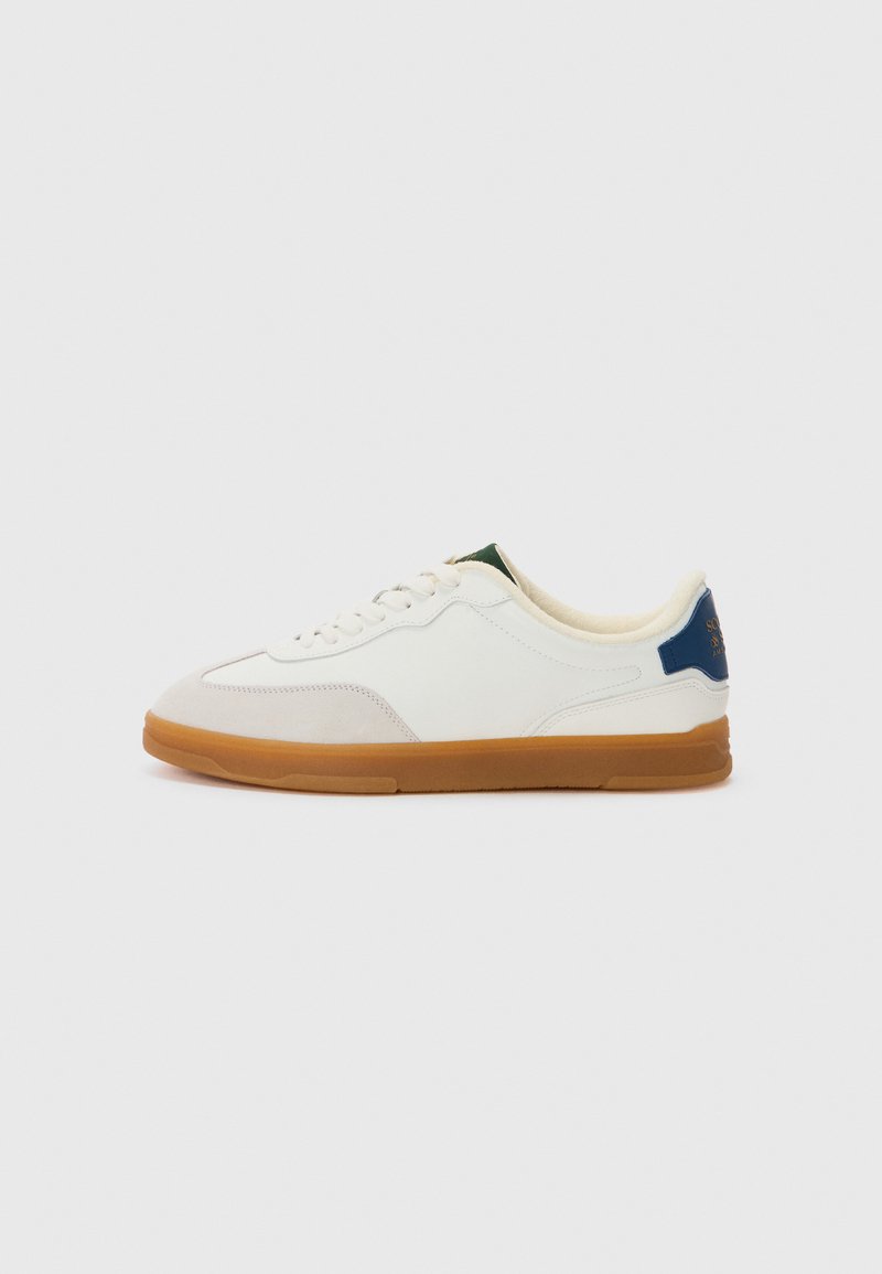 White sneakers with a smooth leather upper, tan gum rubber sole, subtle grey accents, and green and blue detailing on the heel.