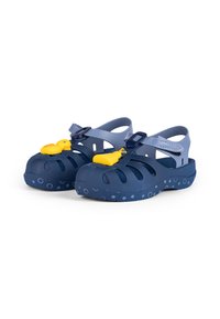 Marineblaue Kunststoff-Clogs mit offenem Design, verziert mit gelben Gummienten und kreisförmigen Mustern auf der Sohle.