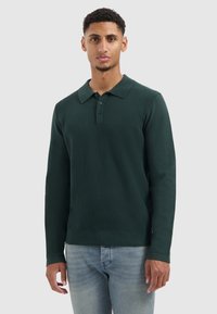 Donkergroen gebreide polo met lange mouwen, klassieke kraag, drie-knopen placket en een gestructureerd patroon aan de voorkant. Zachte stof.