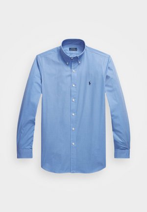 Chemise bleu clair à manches longues en mélange de coton, avec un col pointu, des boutons blancs et un logo brodé sur la poitrine gauche.