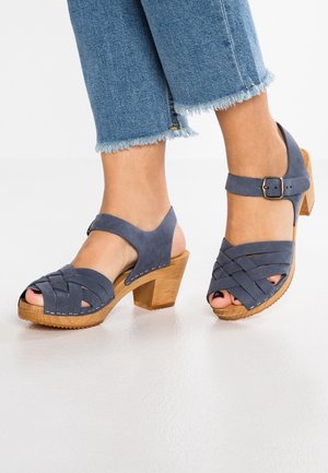 Sandales à talons en suède gris avec un design de sangle tissée, bout ouvert et sangle de cheville. Talon en bois bloc, semelle texturée et détails de couture.