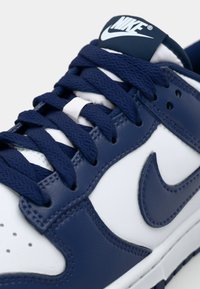 Nike sneaker featuring a white and navy blue leather upper, navy laces, perforations on the toe, and a branded tongue label.
