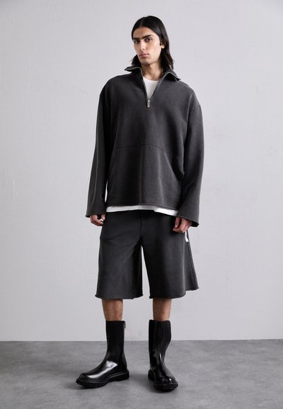 Överdriven mörkgrå fleecepolo med en fjärdedels dragkedja, kombinerad med matchande shorts och svarta ankelstövlar med en slät lädertextur.