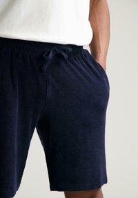 Marineblå terry-klutshorts med elastisk midje og snøring. Har sidelommer og en myk, absorberende tekstur.