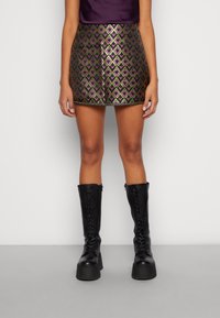 Metalen mini-jurk met een geometrisch patroon in paars en groen, gecombineerd met zwarte veterlaarzen tot de knie. Soepele textuur.