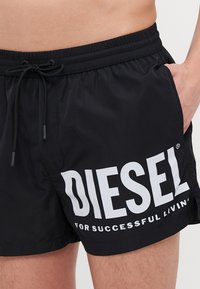Shorts de bain noirs en matériau léger, dotés d'une taille avec cordon de serrage et d'un logo blanc bien visible qui indique "DIESEL POUR UNE VIE RÉUSSIE."