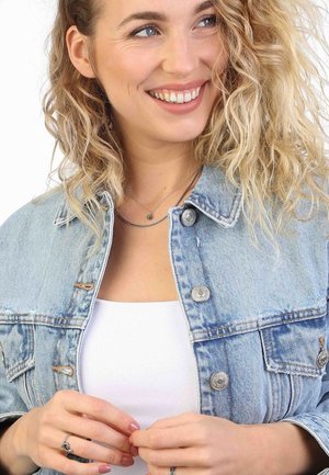 Lichtblauwe denimjacket met zilveren knopen, gedragen over een witte top. Het model heeft krullend haar en draagt gelaagde zilveren kettingen.