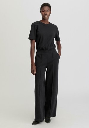 Schwarzes, tailliertes T-Shirt mit kurzen Ärmeln, kombiniert mit hoch taillierten, weiten Hosen in derselben Farbe. Weicher Stoff und schlichtes Design.
