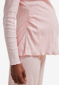 Person wearing ribbed, light pink long-sleeve top and pants with lettuce-edge hems, showing a close-up of the side torso and hand.