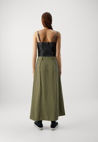 Haut court noir élastiqué avec un dos texturé et de fines bretelles, associé à une longue jupe vert olive et des baskets noires.