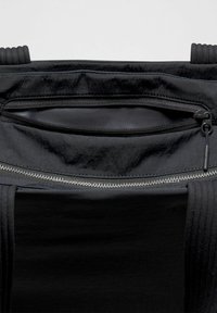 Melnas auduma soma ar divām rāvējslēdzēja kabatām un mīkstinātiem rokturiem, redzama uz vienkārša fona.