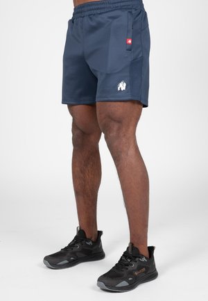 Marineblauwe sportshorts met een elastische tailleband, zijzak en een wit logo. Gecombineerd met zwarte sneakers met een gevarieerd ontwerp en grijze accenten.