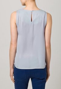 Ljusgrå ärmlös topp med en nyckelhålöppning på baksidan och en slät struktur, kombinerad med mörkblå figurnära byxor.