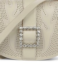 Bolso beige con diseño perforado y un cinturón cuadrado de strass. Presenta una textura suave y una correa ajustable de tamaño medio.