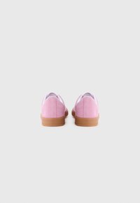 Rosa mockaskinnsneakers med lågt skaft och bruna gummisulor. Har rundad bakdel och vit inredning. Slät textur.