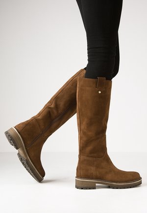 Brązowe zamszowe kozaki za kolano z bocznym zamkiem i profilowaną podeszwą, noszone z czarnymi dopasowanymi spodniami, przedstawione na białym tle.