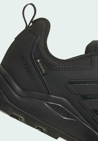 Zapato de senderismo negro con parte superior texturizada, etiqueta GORE-TEX, suela acolchada con un patrón de treads distintivo y tab de refuerzo en el talón.