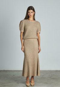 Completo in maglia a due pezzi con un top beige testurizzato e maniche a sbuffo, abbinato a una gonna che si allarghi sul bordo. Tacchi chunky completano il look.