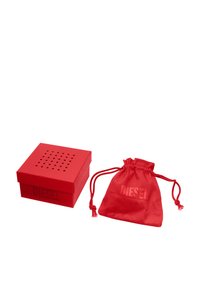 Scatola quadrata rossa con coperchio perforato, logo "DIESEL" in rilievo; accompagnata da un sacchetto rosso con cordoncino abbinato con lo stesso logo.