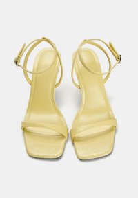 Gelbe High Heels Sandalen mit quadratischen Zehen, dünnen Knöchelriemen und strukturiertem Kunstlederfinish. Mit einer glatten, glänzenden Sohle.