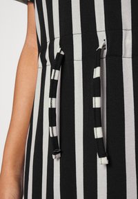 O material da vestimenta com riscas pretas e brancas apresenta uma cintura elástica com cordões, tecido texturizado e um acabamento suave.