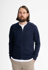 Dunkelblaues Zip-Cardigan aus weichem Strickmaterial. Verfügt über gerippte Bündchen und Saum, hat einen runden Halsausschnitt und ein minimalistisches Design.