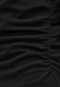 Κοντινή λήψη μαύρου υφάσματος με λεπτομέρεια ρυτίδωσης που δημιουργεί υφή με οριζόντιες πτυχώσεις.