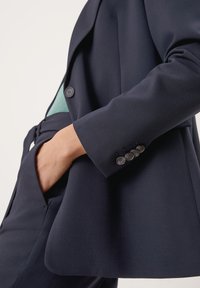 Marineblazer met een getailleerde pasvorm, een enkele knoopsluiting, 4-knopen manchetten en zakdetails. Glad materiaal met een gestructureerde silhouet.
