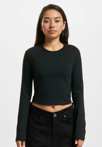Crni dugi rukav uski crop top od mekog materijala. Ima okrugli izrez i uski siluetu, u kombinaciji s crnim trapericama visokog struka.