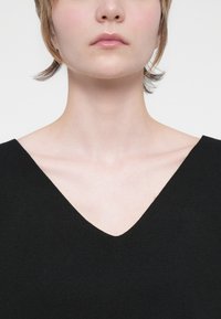 Čierny pulóver s výstrihom do V, vyrobený z mäkkej tkaniny, s čistým, minimalistickým dizajnom, hladkou textúrou a jemnými kontúrami.