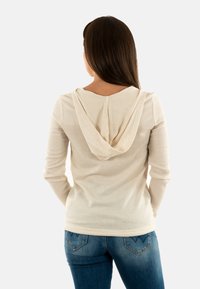 Haut à capuche crème à manches longues avec une coupe décontractée, associé à un jean bleu taille moyenne avec un design de poche arrière décoratif.