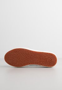 Semelle de sneaker blanche avec une base en caoutchouc orange texturé, présentant une forme arrondie et une semelle à motif pour une meilleure adhérence.