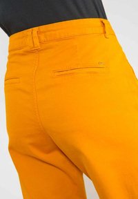 Orangefarbene Hose mit glatter Textur und taillierter Passform. Verfügt über zwei Gesäßtaschen und einen kleinen Logo-Akzent in der Nähe des Bundes.