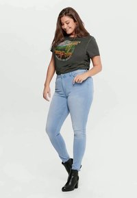 Σκούρο γκρι γραφικό μπλουζάκι με σχέδιο φύσης, συνδυασμένο με ανοιχτό μπλε στενά τζιν και μαύρες γοβέτες με ασθενή τακούνι. Λείες υφές υφασμάτων.