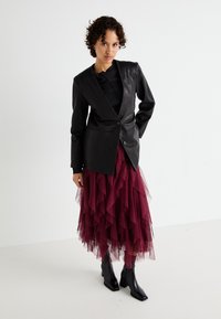 Svart läderblazer med en enda knapp, kombinerad med en burgundy volangkjol i tyl. Outfiten har ankelstövlar och en lagerdesign.